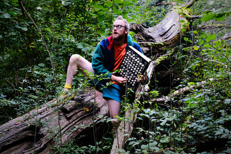 s.panrucker holding a synthesizer in the woods, looking slightly spooked as if a wolf is trying to steal his frequencies